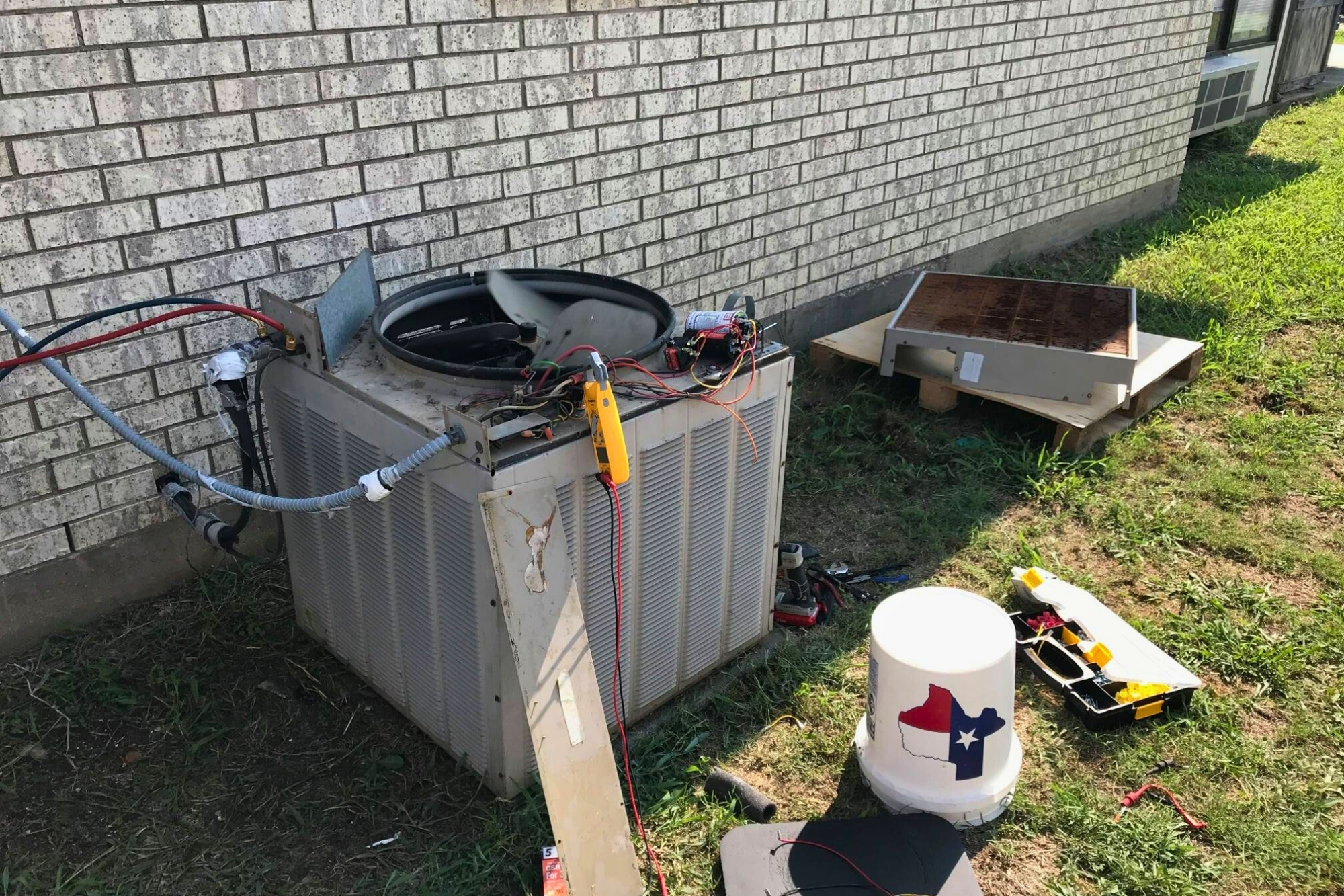 Outdoor HVAC unit under repair with tools on the ground